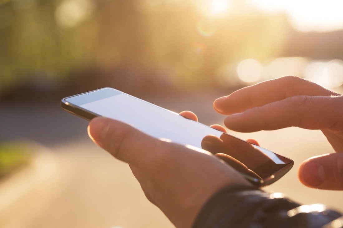 Close-up of a hand on a mobile phone, ready to call for a glass repair estimate.