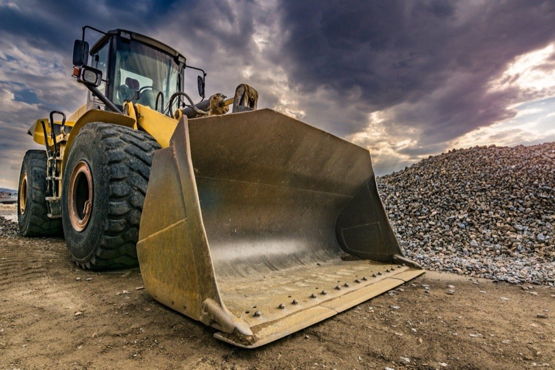 A yellow front loader parked on a gravel site under a dramatic sky.