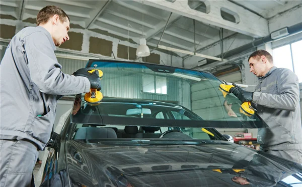 Two J & F technicians setting a new windshield into a car inside the shop.